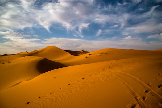 Stunning sand dunes in a desert under a beautiful blue sky with clouds.