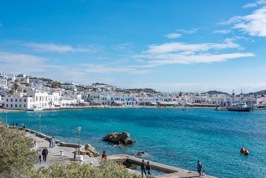 Beautiful view of Mykonos town with people strolling by the blue Aegean Sea.