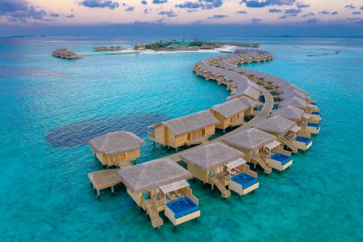 Aerial view of luxurious water villas overlooking turquoise water and a pristine island in the Maldives.