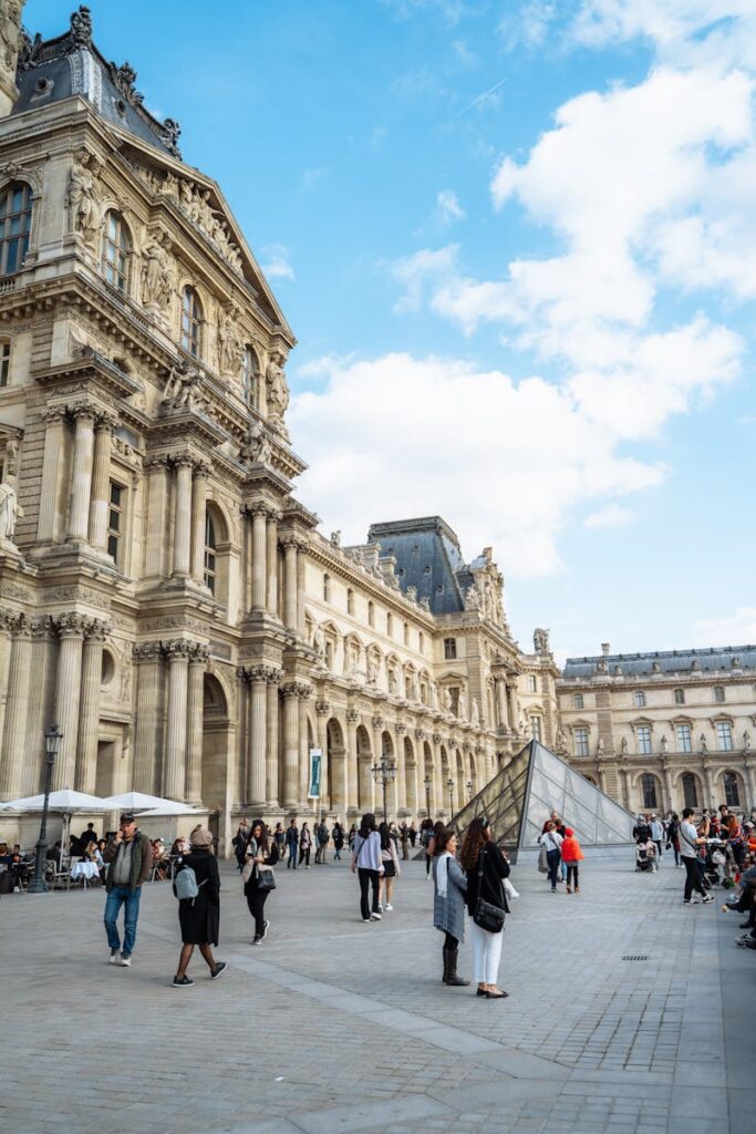 The Louvre Museum's grand architecture and bustling plaza captured in vibrant daylight, Paris.