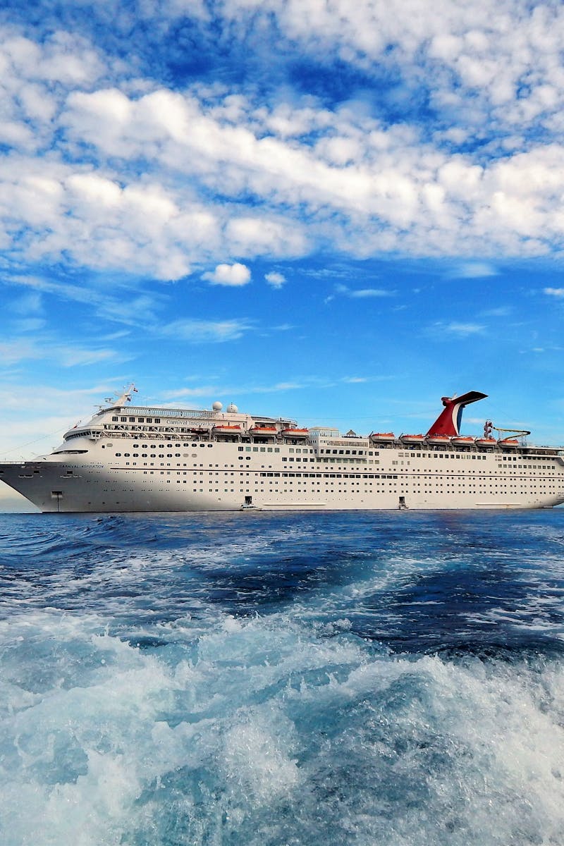 A majestic cruise ship sails on the open sea beneath a vivid blue sky, framed by white clouds.